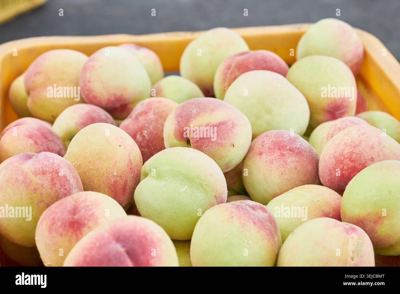 Le foto mostrano pesche all'inizio dell'estate in casse gialle e patate novelle in ciotole rosse in un mercato locale, catturando l'autentico fascino del prodo crudo di stagione Foto Stock