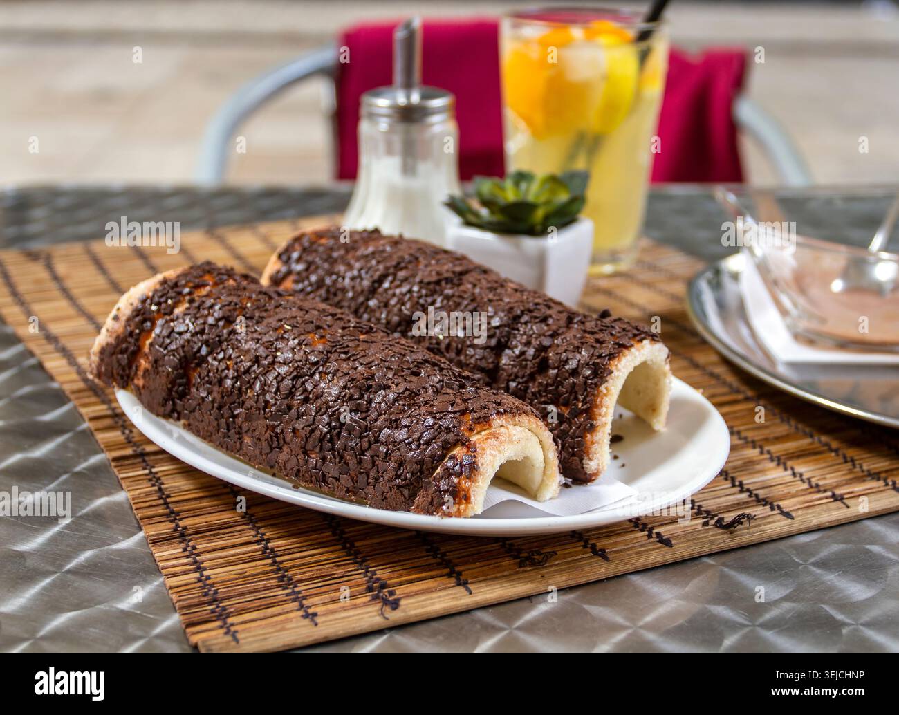 Due tortine a camino al cioccolato Kurtoskalacs con granella di cioccolato servite su un piatto bianco con limonata fresca su un tavolo di un caffè a Budapest, Ungheria Foto Stock