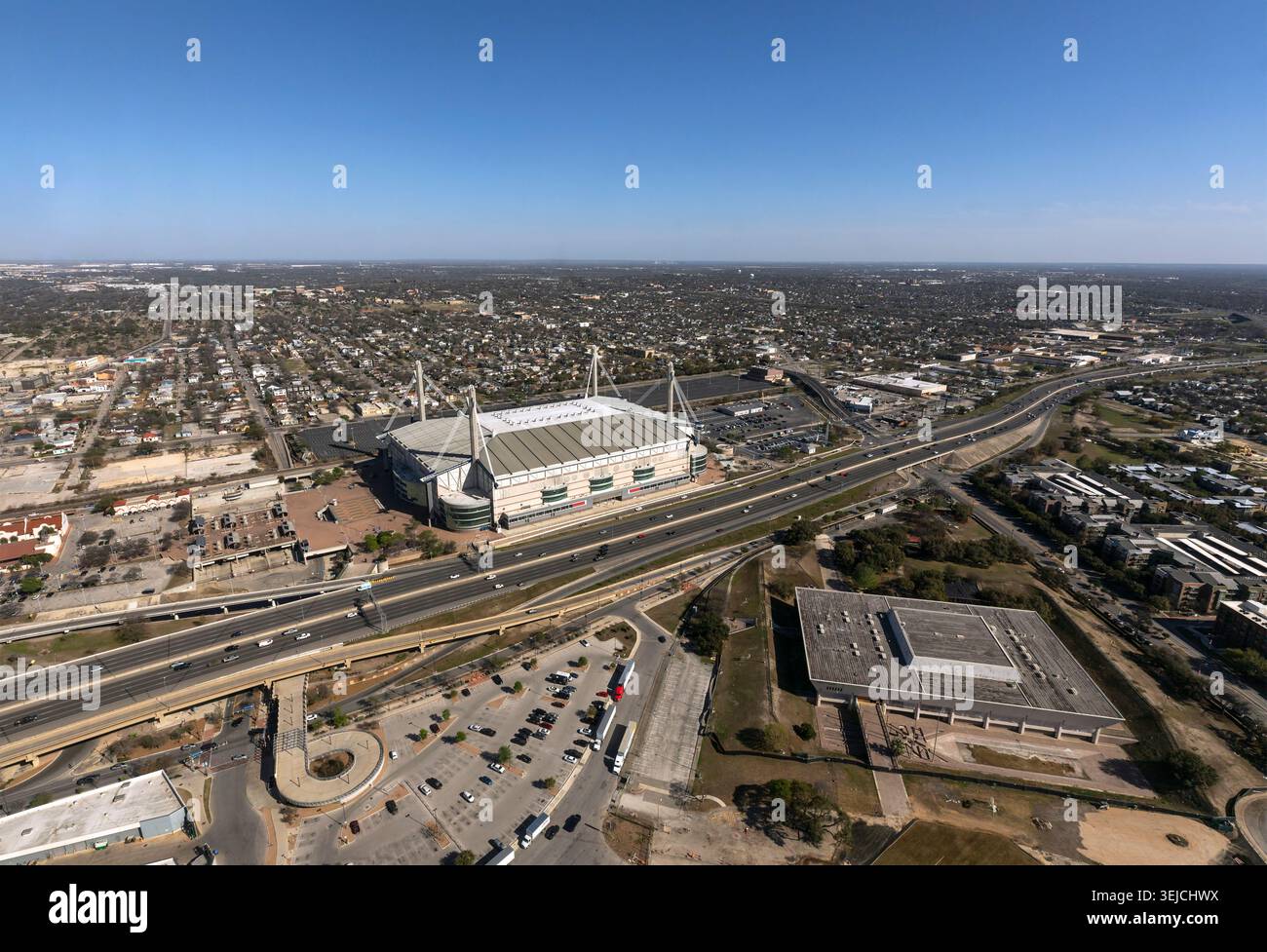 Veduta aerea mostra lo stadio Alamodome accanto a un'autostrada con parcheggi e espansione urbana sotto un cielo blu a San Antonio, Texas, USA Foto Stock