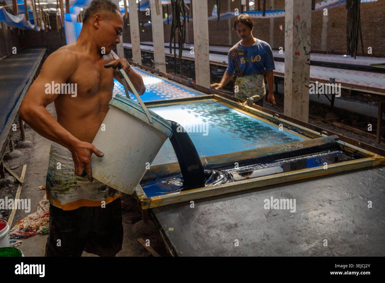 Un operaio versa una tintura tessile su un tavolo da serigrafia in una bottega nel villaggio di Laban, Mojolaban, Sukoharjo, Indonesia. Foto Stock