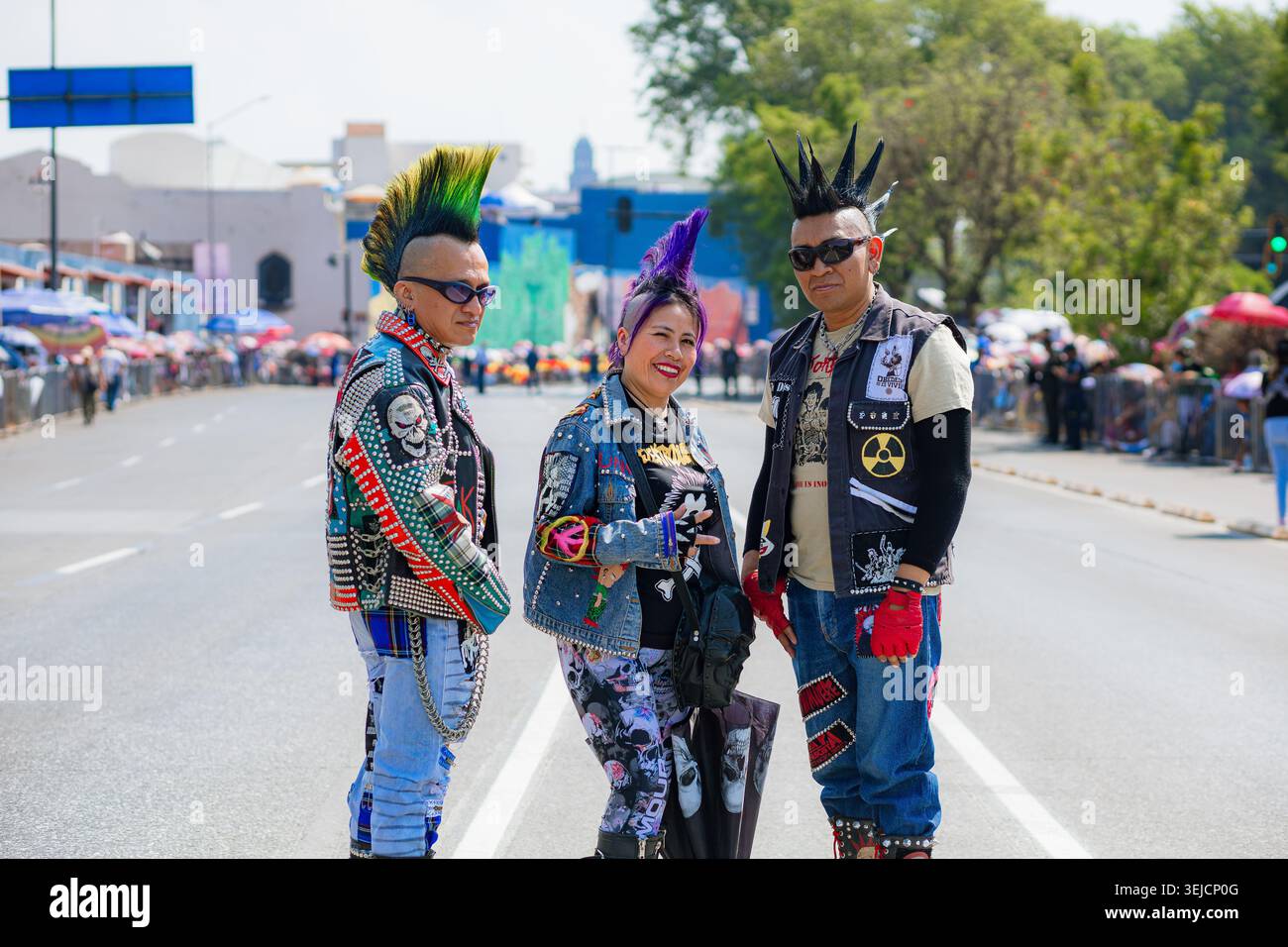 Un gruppo di tre amici punk con colorate acconciature mohawk sorridono alla telecamera durante un evento urbano all'aperto. Foto Stock