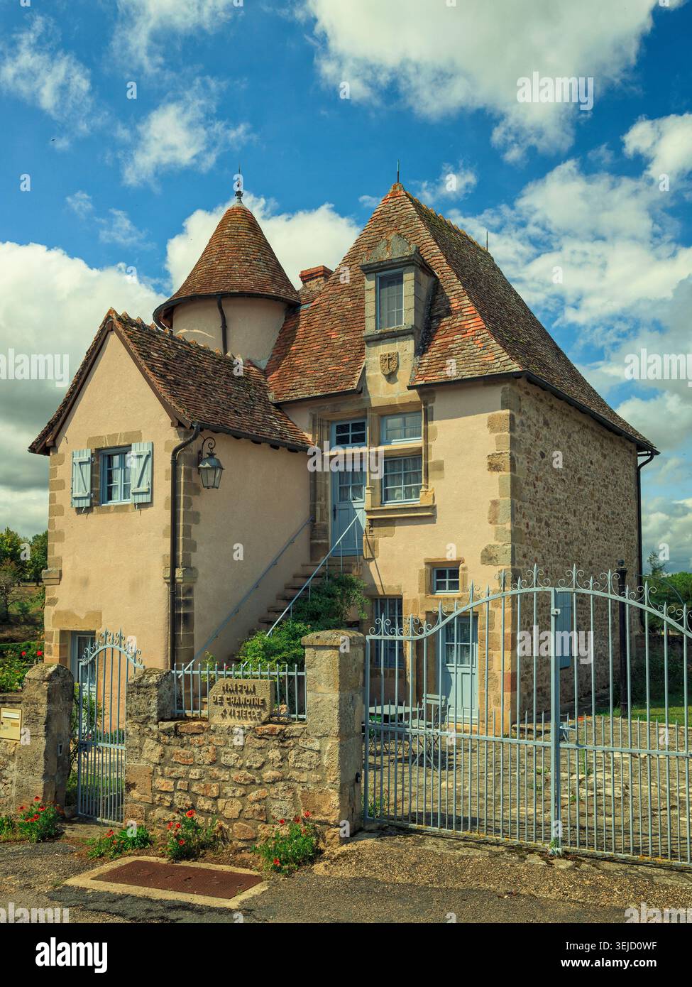 Bourbon-l'Archambault, Francia - 15.08.2023: Affascinante residenza in stile medievale con torretta e persiane blu dietro un cancello metallico Foto Stock