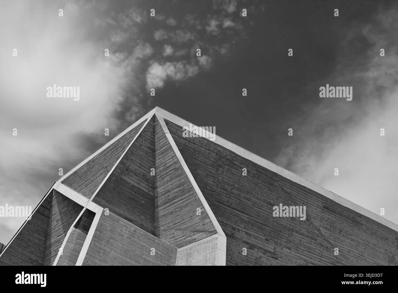 Moderna architettura brutalista in cemento con linee geometriche contro il cielo drammatico. Foto Stock