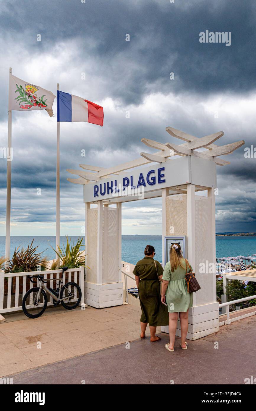 Persone che guardano un menu sotto nuvole scure lungo il lungomare di Nizza, Nizza, Provenza-Alpi-Costa Azzurra, Alpi-Maritimes, Francia Foto Stock