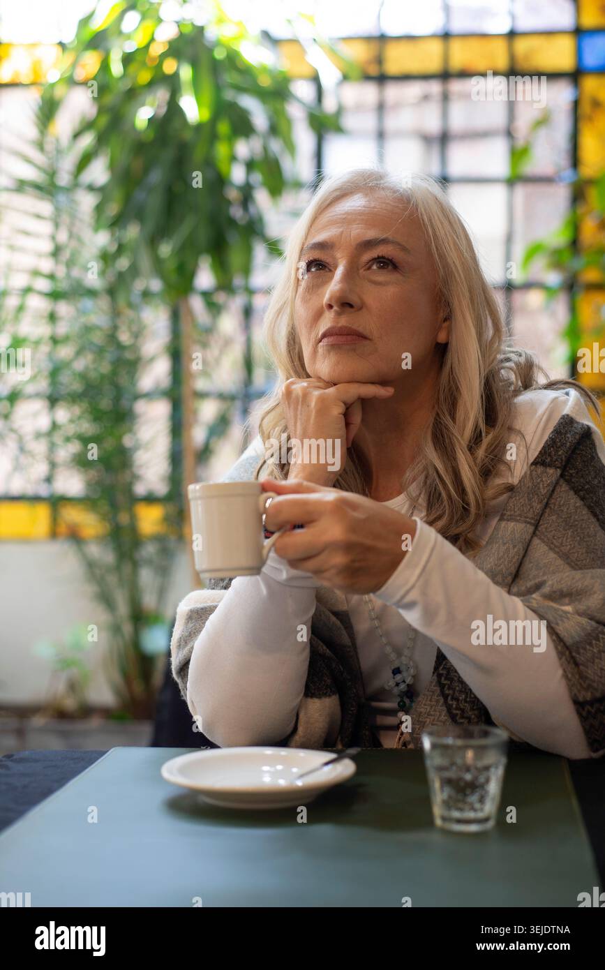 Donna matura che tiene in mano una tazza di caffè con un'illuminazione soffusa Foto Stock