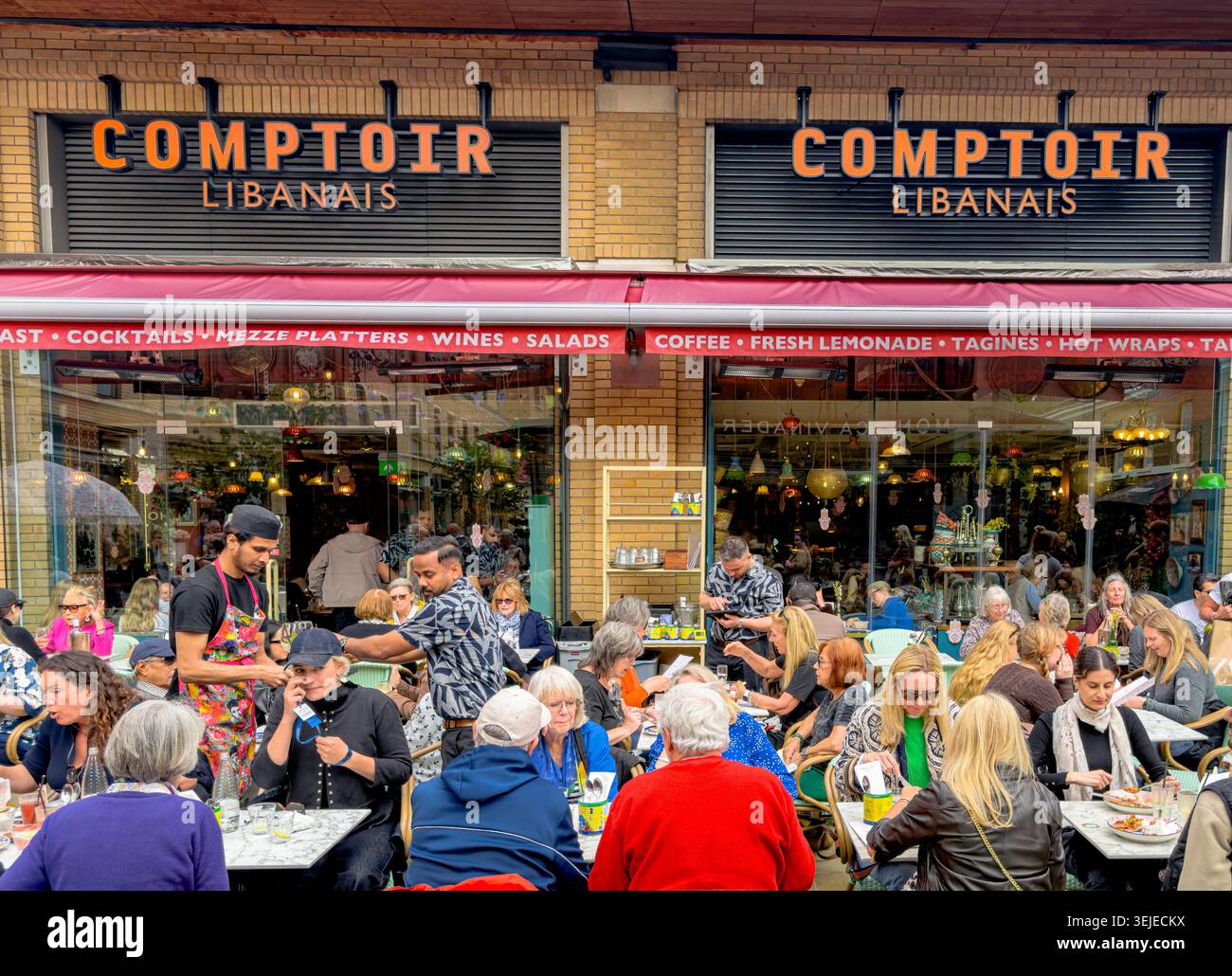 Le persone sedute all'esterno gusteranno il pranzo in una giornata di primavera in un affollato Comptoir Libanais, un ristorante di cucina mediorientale in Duke of York Square, Londra, Regno Unito Foto Stock