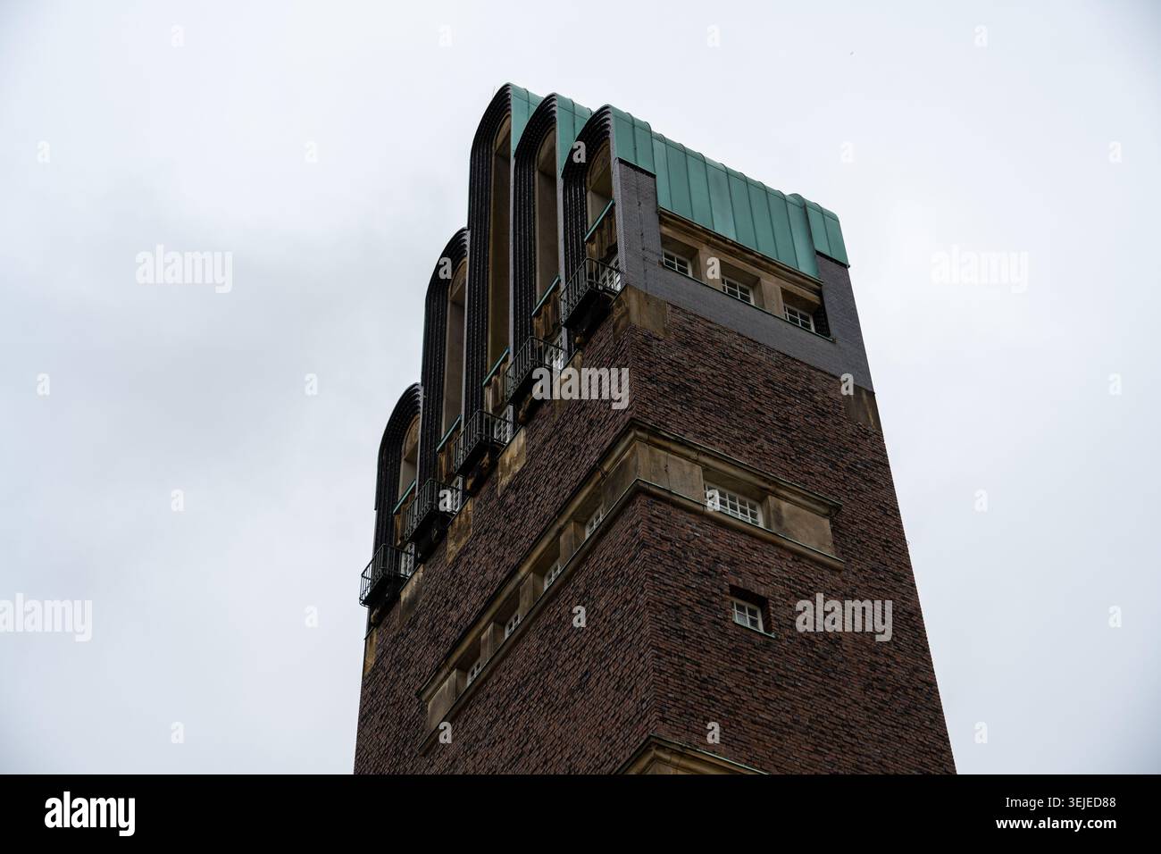Angolo verso l'alto della sezione superiore di Hochzeitsturm con aperture ad arco e dettagli del tetto in rame verde contro un cielo nuvoloso a Darmstadt, Germania. Foto Stock