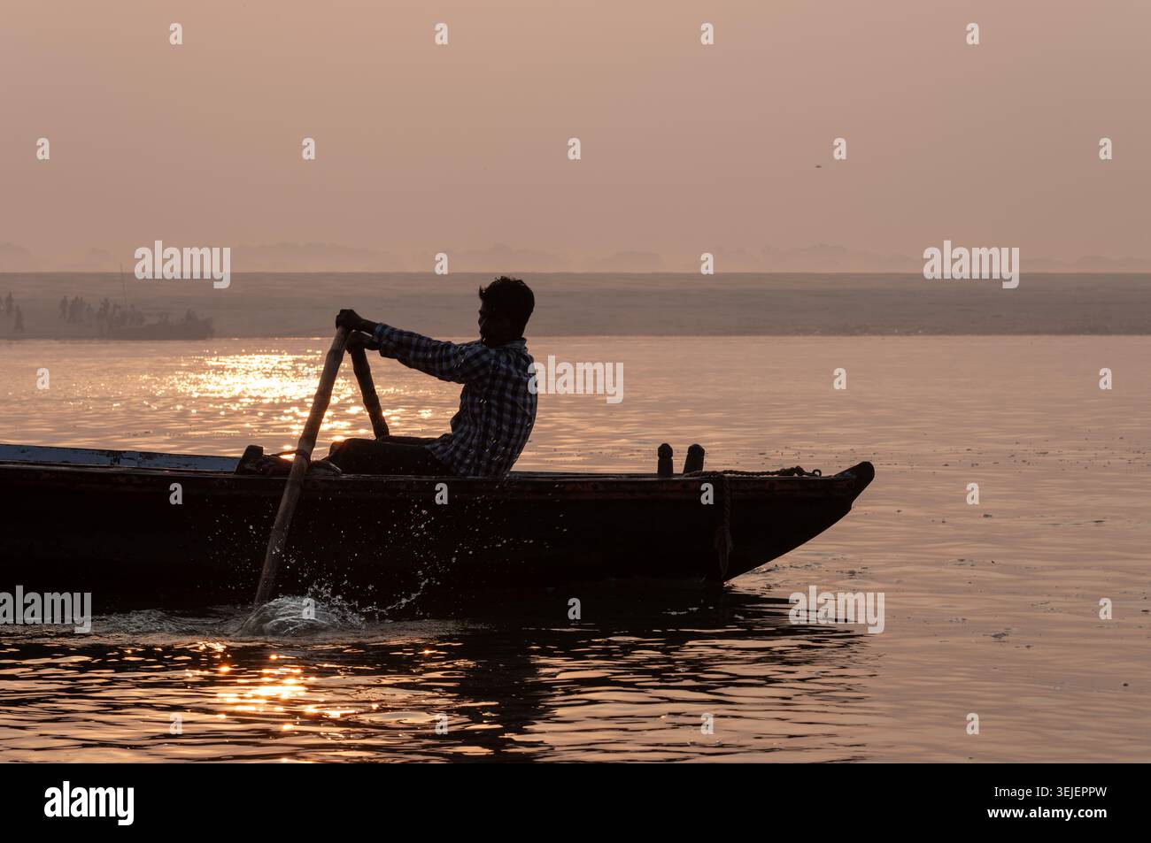 Silhouette di un barcaiolo che canta una tradizionale barca di legno all'alba sul Gange, Varanasi, Uttar Pradesh, India. Foto Stock