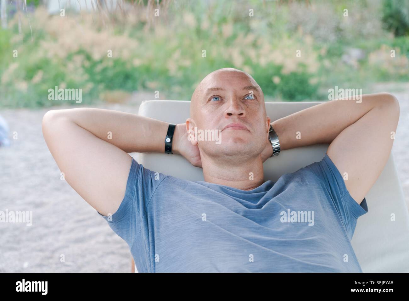 Il primo piano dell'uomo calvo caucasico guarda in alto rilassandosi con le braccia dietro la testa sulla sdraio. Adatto per un ritiro di meditazione, un marchio di benessere e uno stile di vita all'aperto Foto Stock