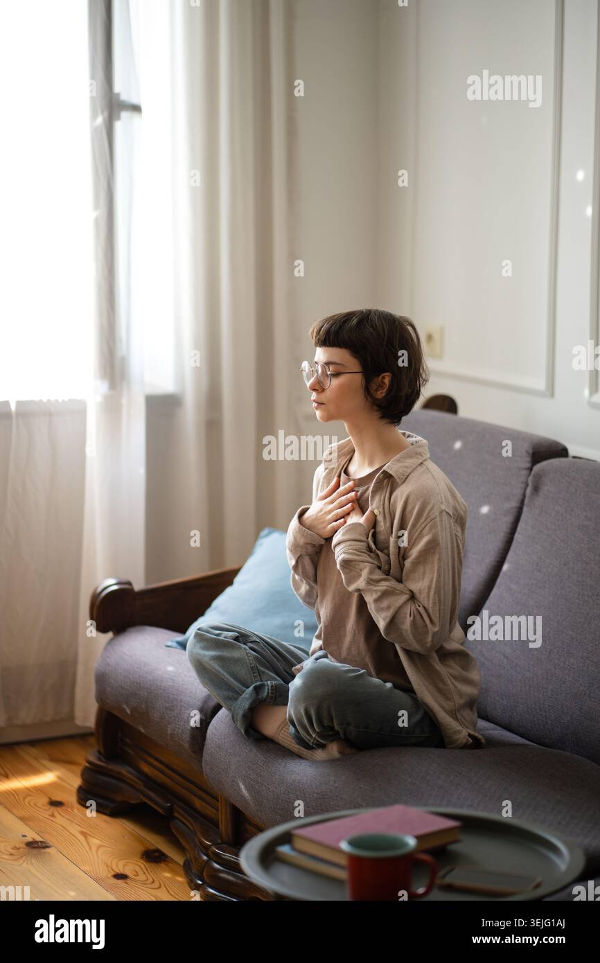 Giovane donna seduta sul divano che pratica la meditazione, fa esercizi respiratori per rilassare i pensieri. Foto Stock