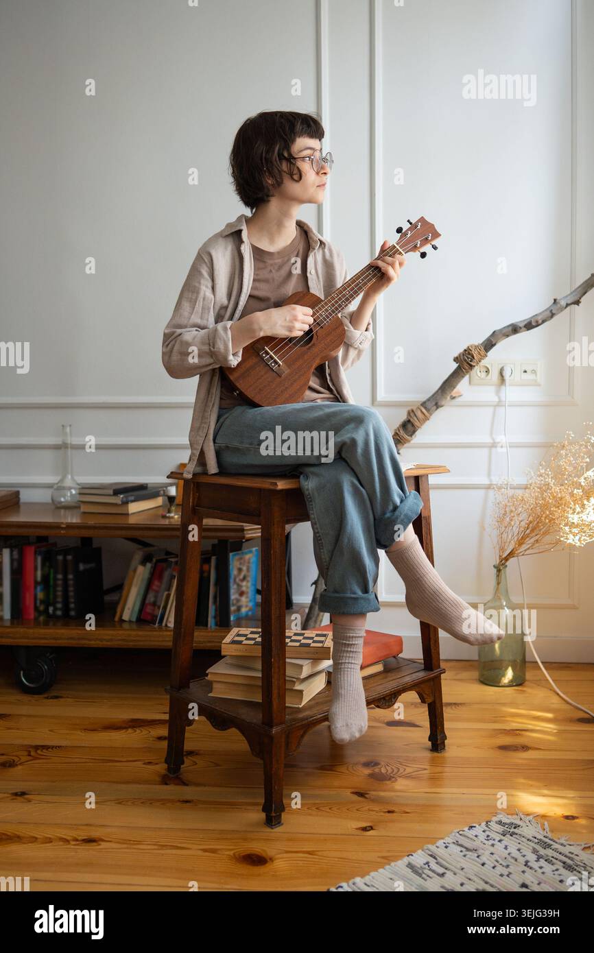 Giovane donna creativa che suona musica con la chitarra acustica ukulele e si gode la musica a casa durante il fine settimana. Foto Stock