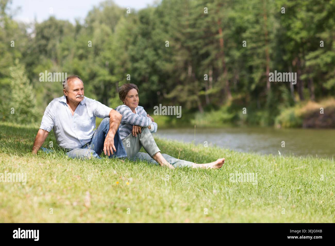 Felice coppia anziana seduta d'estate vicino al lago Foto Stock