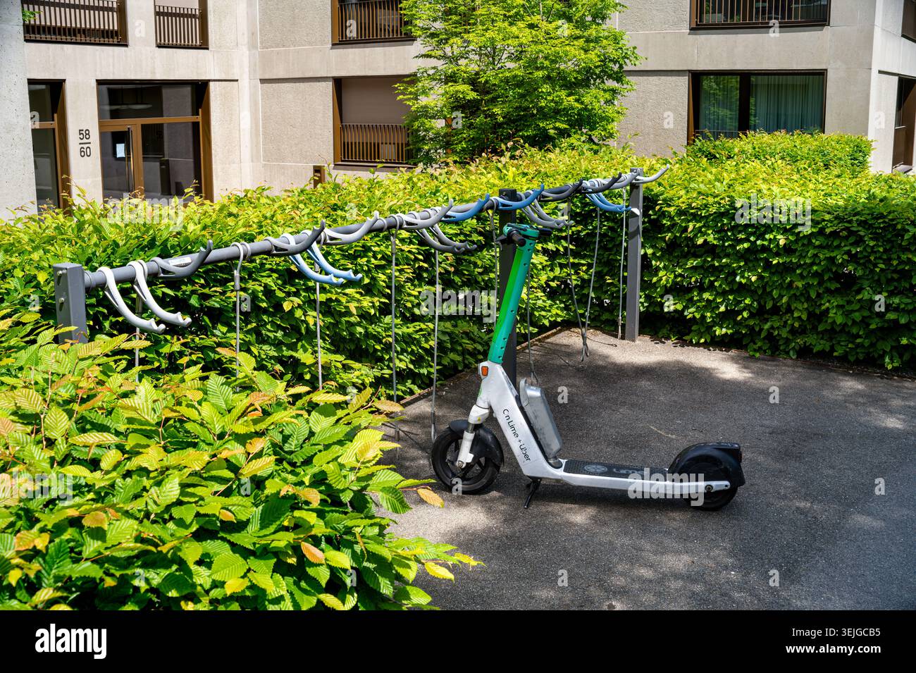 Zurigo, Svizzera - 21 maggio 2026: Scooter elettrico parcheggiato vicino a un portabiciclette accanto a una siepe e a un condominio in una tranquilla zona residenziale su un Foto Stock