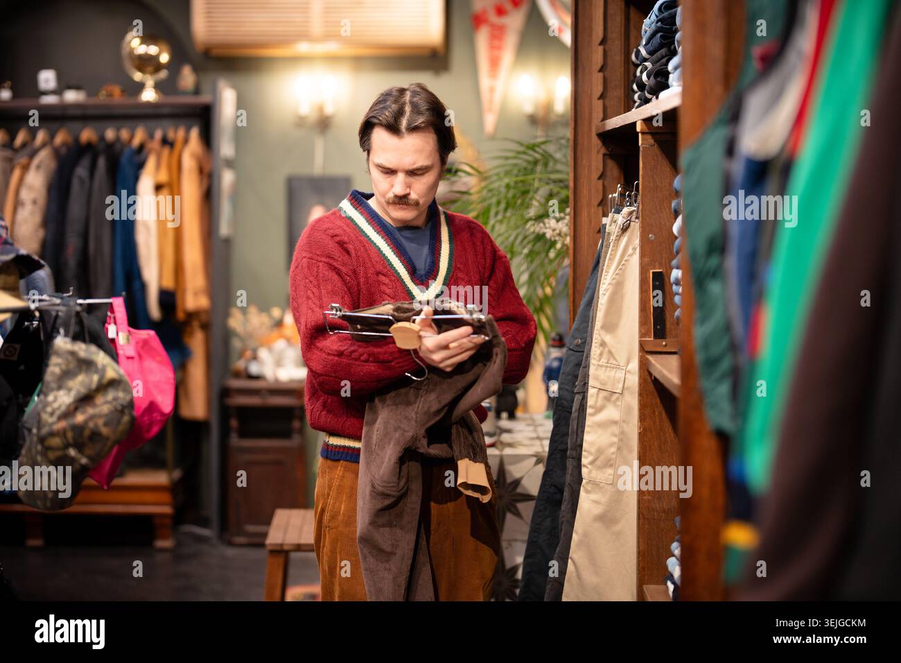 Un cliente alla moda attento all'uomo hipster che sceglie pantaloni di velluto alla moda in un negozio vintage di seconda mano. Foto Stock