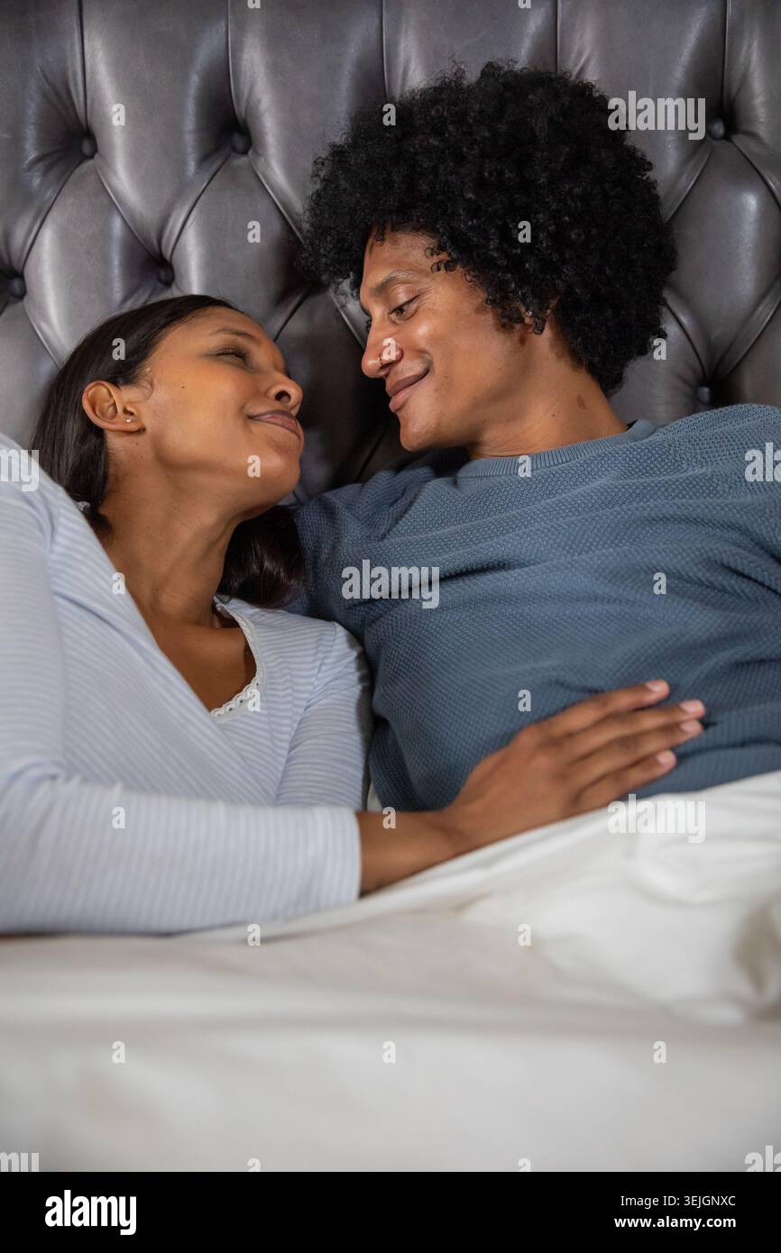 Diverse coppie che si trovano fianco a fianco sul letto con piumone bianco su testiera tufted grigio scuro. Romantico, intimo, relax, co Foto Stock