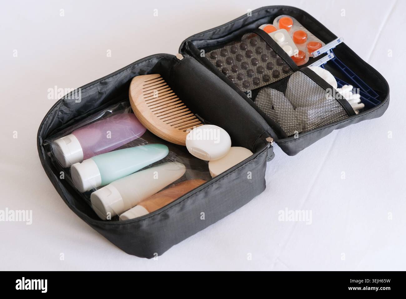 Kit cosmetico da viaggio nero sul letto. flaconi cosmetici colorati confezionati in sacchetto di plastica, pillole e articoli igienici per i viaggi Foto Stock