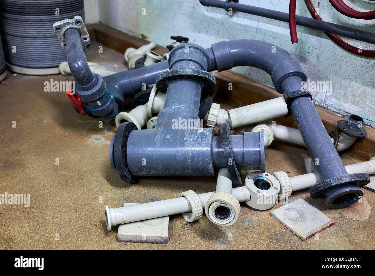 Una pila smontata di tubi e raccordi industriali in PVC grigio e bianco sul pavimento di un'officina. Foto Stock