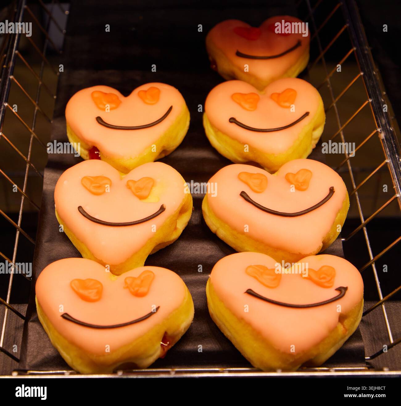Ciambelle di San Valentino a forma di cuore con volti sorridenti e occhi a cuore su un vassoio Foto Stock