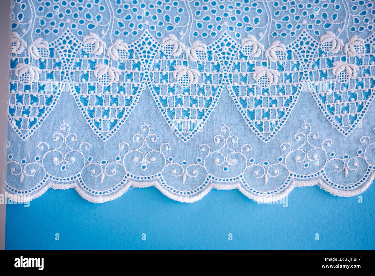 Motivo in pizzo, dettaglio di una tovaglia isolata su sfondo blu. Confine artistico. Artigianato, vintage. Concetto di hobby. Vista dall'alto. Foto Stock
