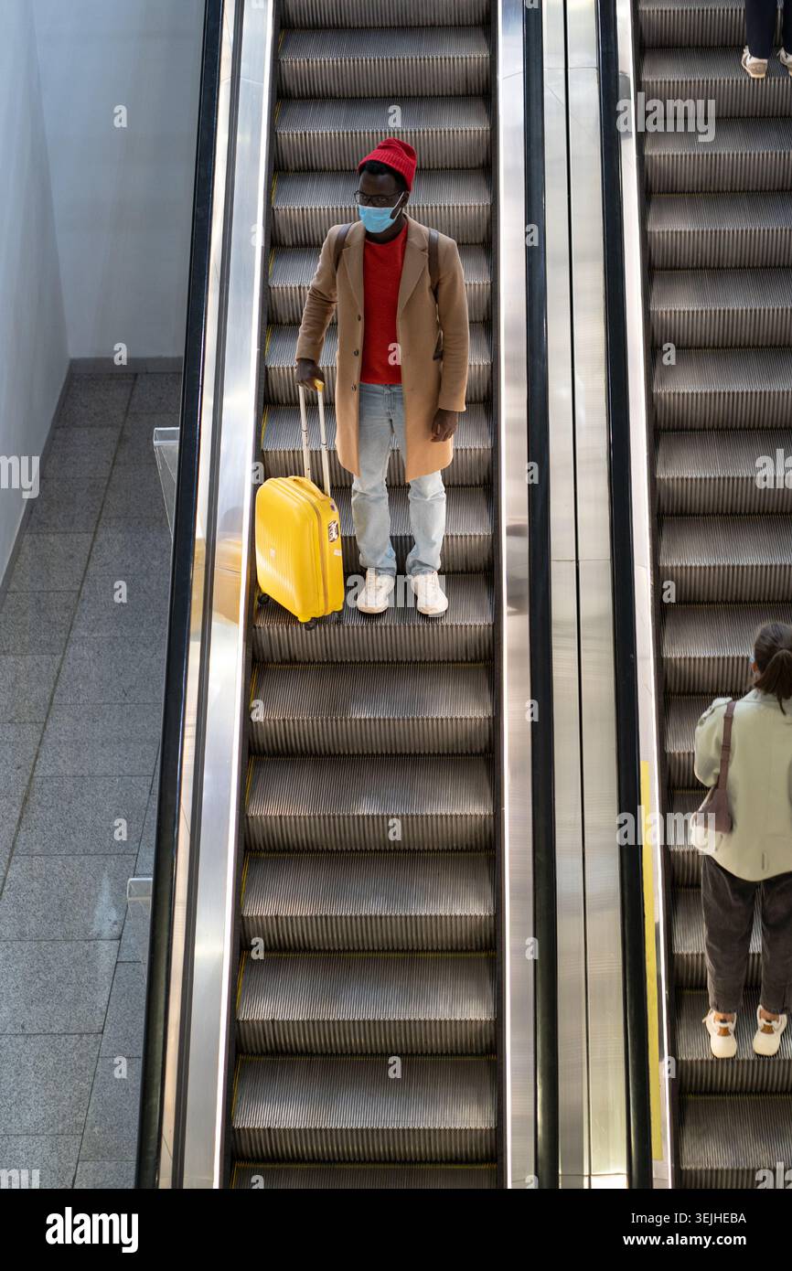 Uomo nero sta su scala mobile in aeroporto indossare maschera per proteggere dal contatto con il virus Nipah Foto Stock