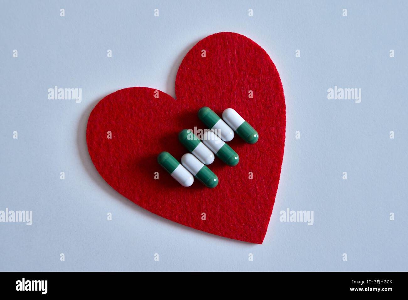 Capsule mediche verdi e bianche disposte su un cuore in feltro rosso a forma di sfondo bianco. Foto Stock