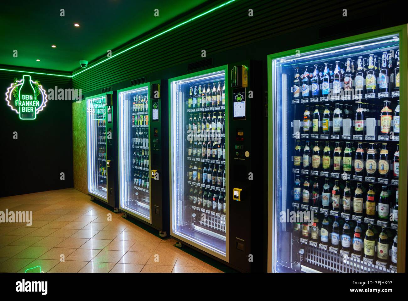 Una fila di moderni distributori automatici di birra con fronte in vetro illuminati con luci LED bianche e verdi. Foto Stock