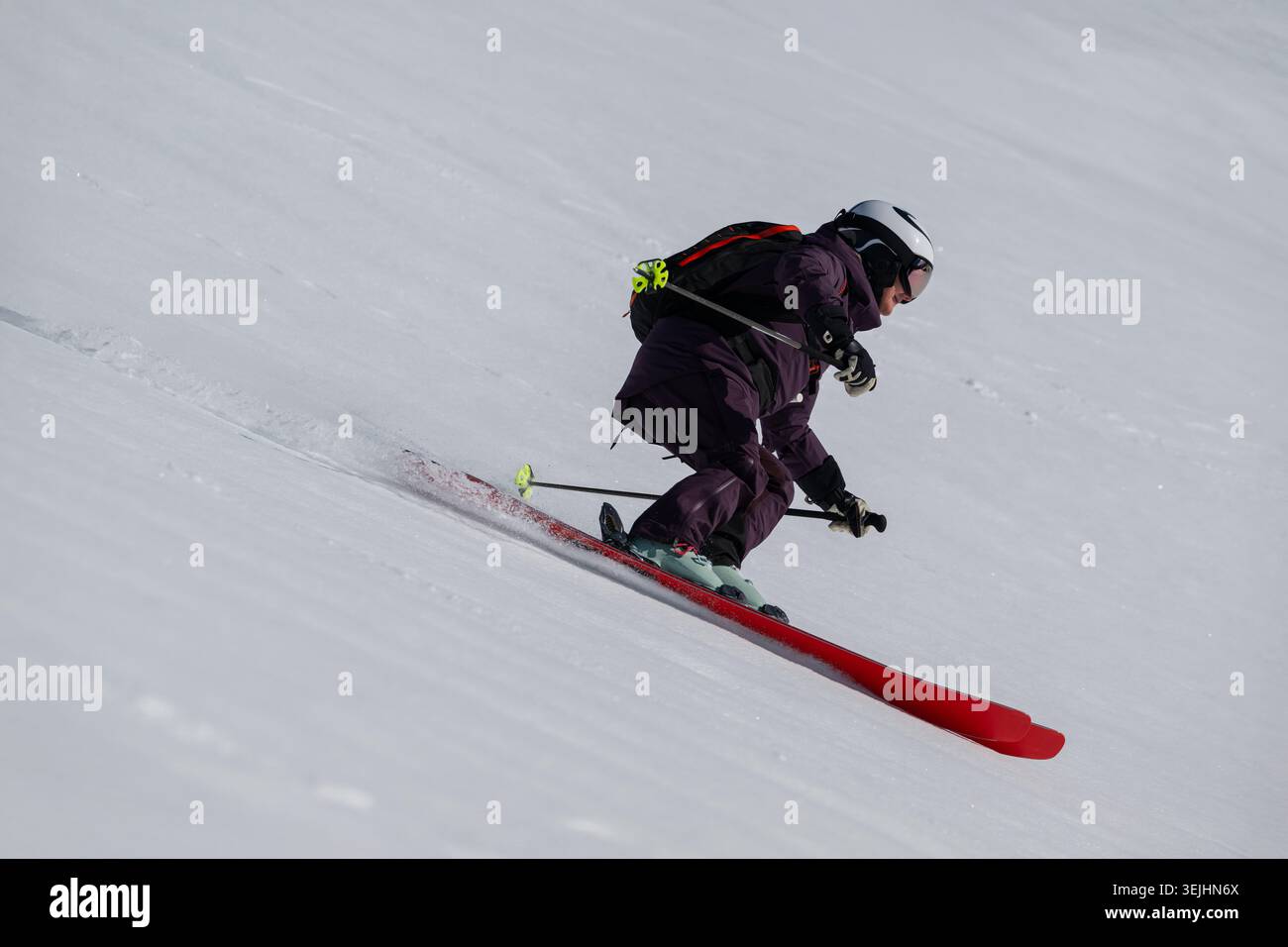Sciatore con attrezzatura viola che percorre una pista innevata con casco e zaino in una giornata intensa Foto Stock