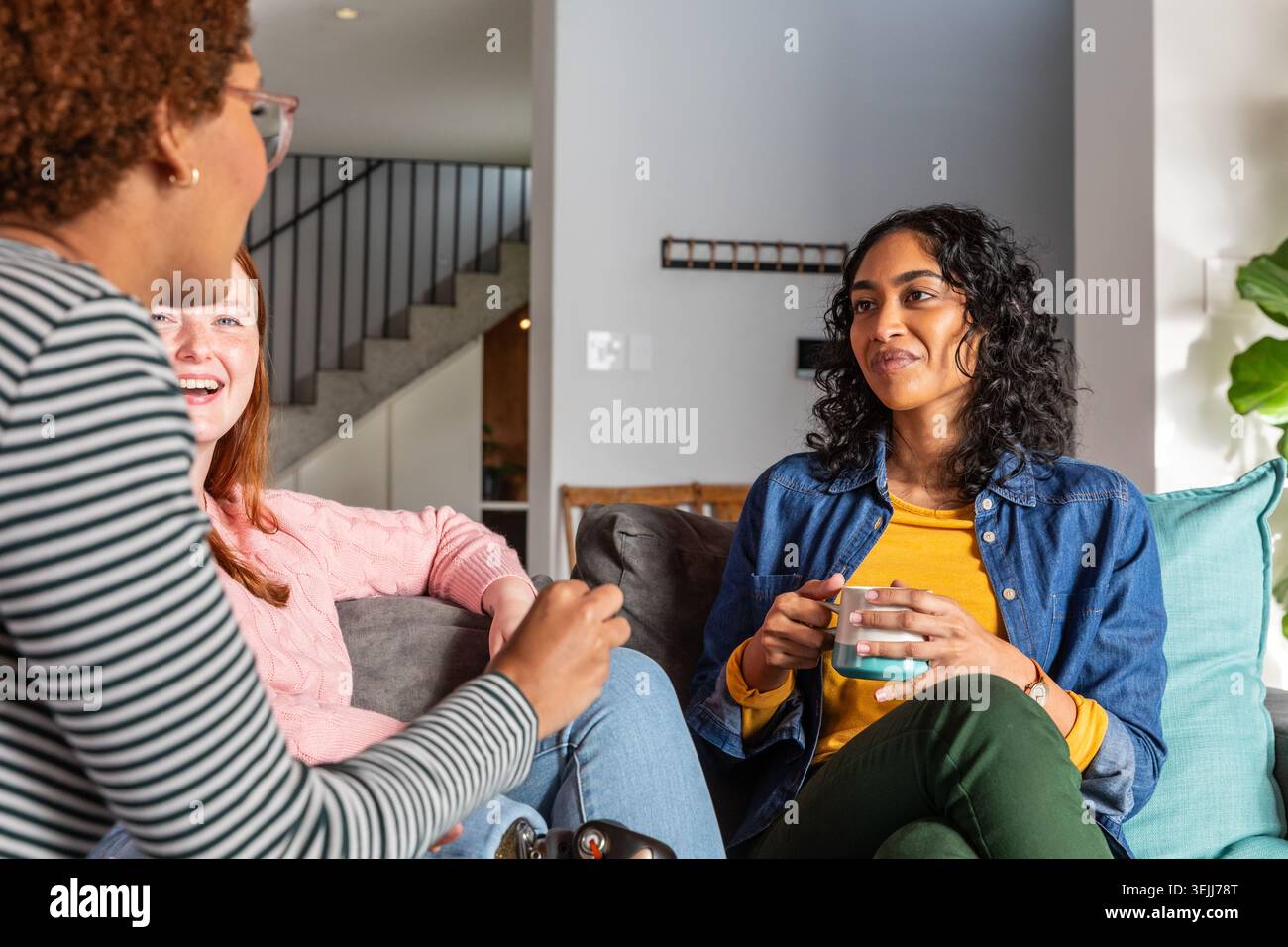 Vari amici sono seduti su un divano in un moderno soggiorno, tenendo in mano tazze e cuscini in ceramica. Amicizia, rel Foto Stock