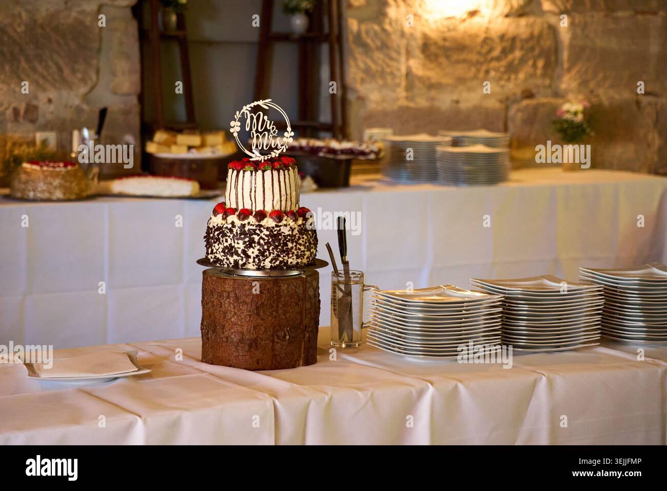 Torta nuziale a più livelli con un topper "Mr & Mrs" su una tribuna di legno a un buffet di ricevimento. Foto Stock