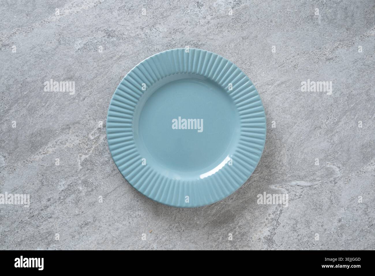 Piastra in ceramica blu vuota su sfondo in pietra grigia. Mockup minimo per la preparazione del tavolo per la presentazione dei piatti, il design dei menu, i blog delle ricette e il branding dei ristoranti Foto Stock