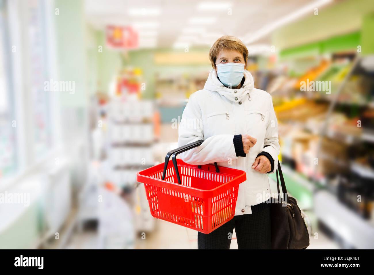Donna anziana che indossa la maschera medica con un cestino della spesa nel supermercato. Foto Stock