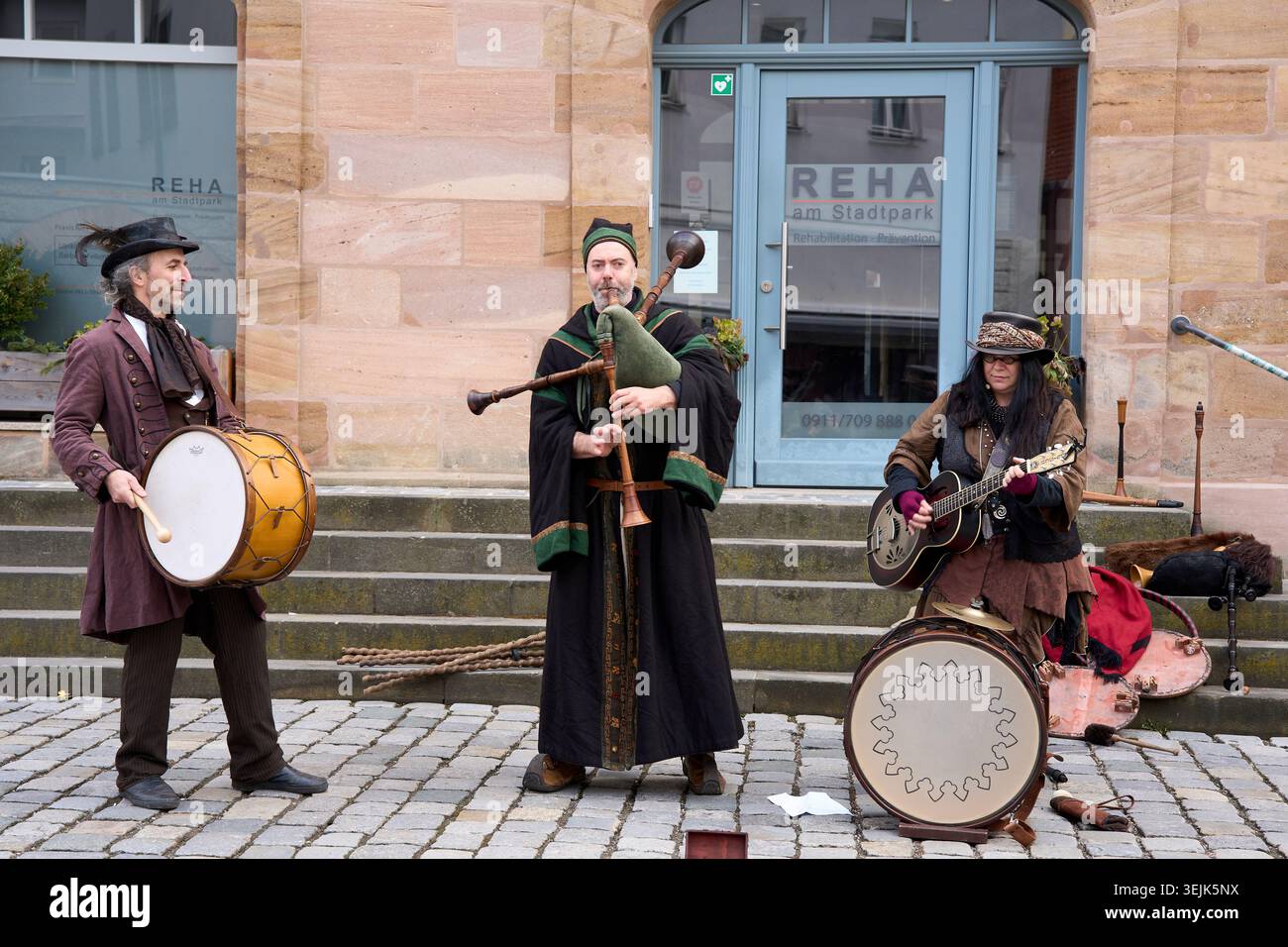 Musicisti di strada in costumi storici che suonano cornamusa, batteria e chitarra in una strada acciottolata. Foto Stock