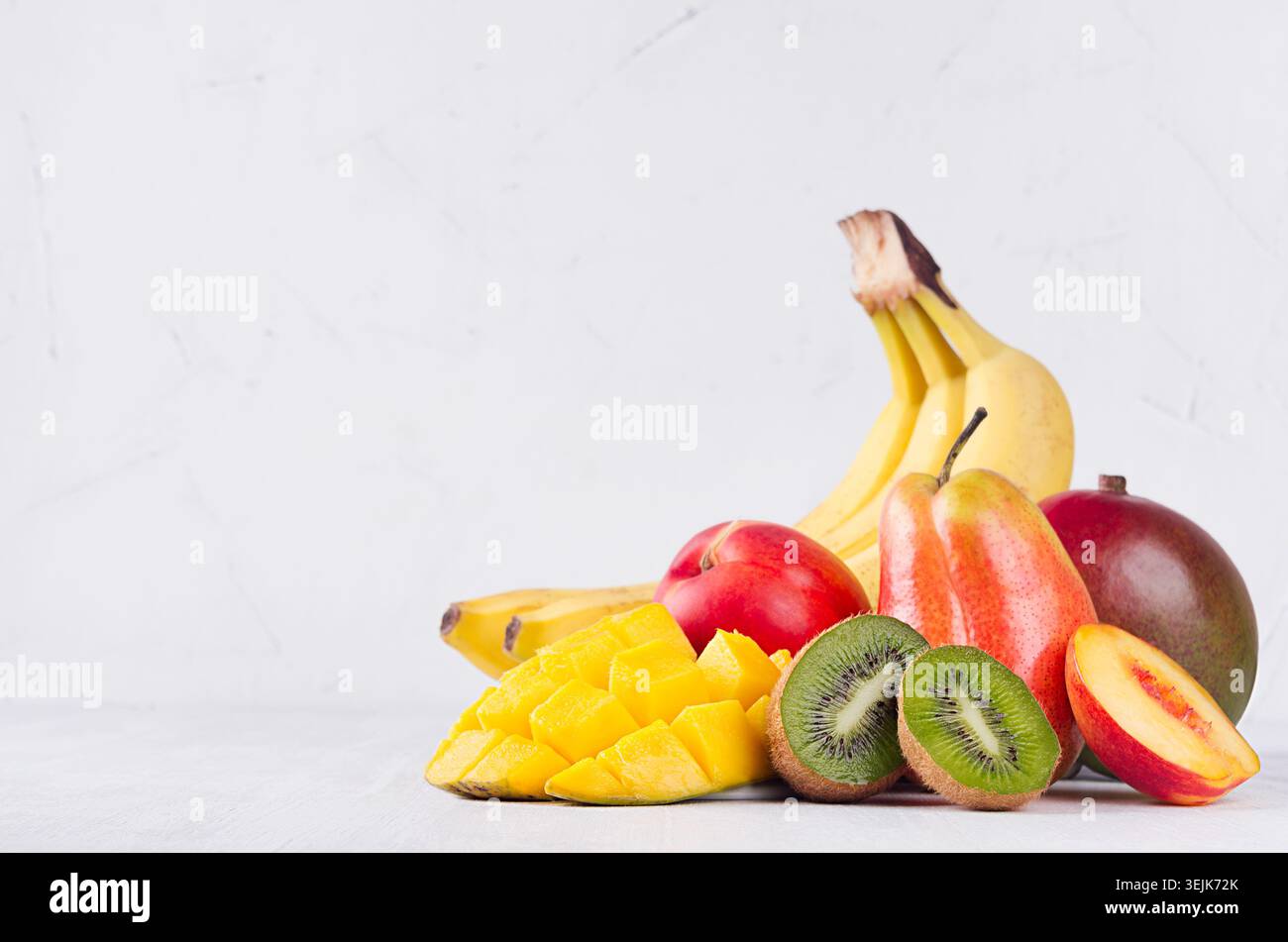 Mix di frutta colorata - frutta intera e succose fette a fette - mango, banana, pera, pesca, kiwi, nactarina su soffice ba di legno bianco Foto Stock