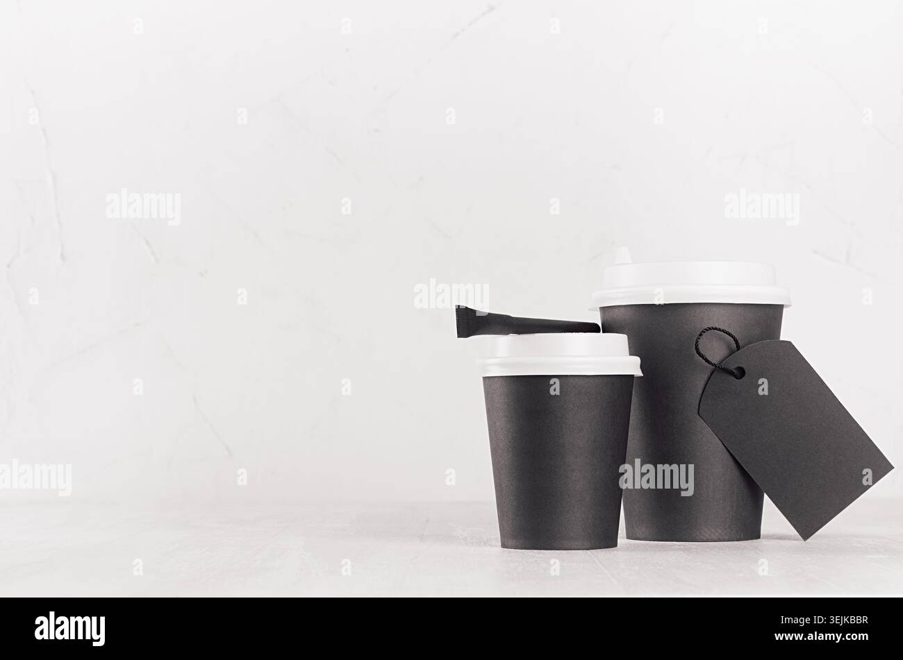 Mockup caffè - due tazze di carta nera con tappi bianchi, etichetta vuota e sacchetto di zucchero su un tavolo di legno bianco con spazio per le copie, caffetteria Foto Stock