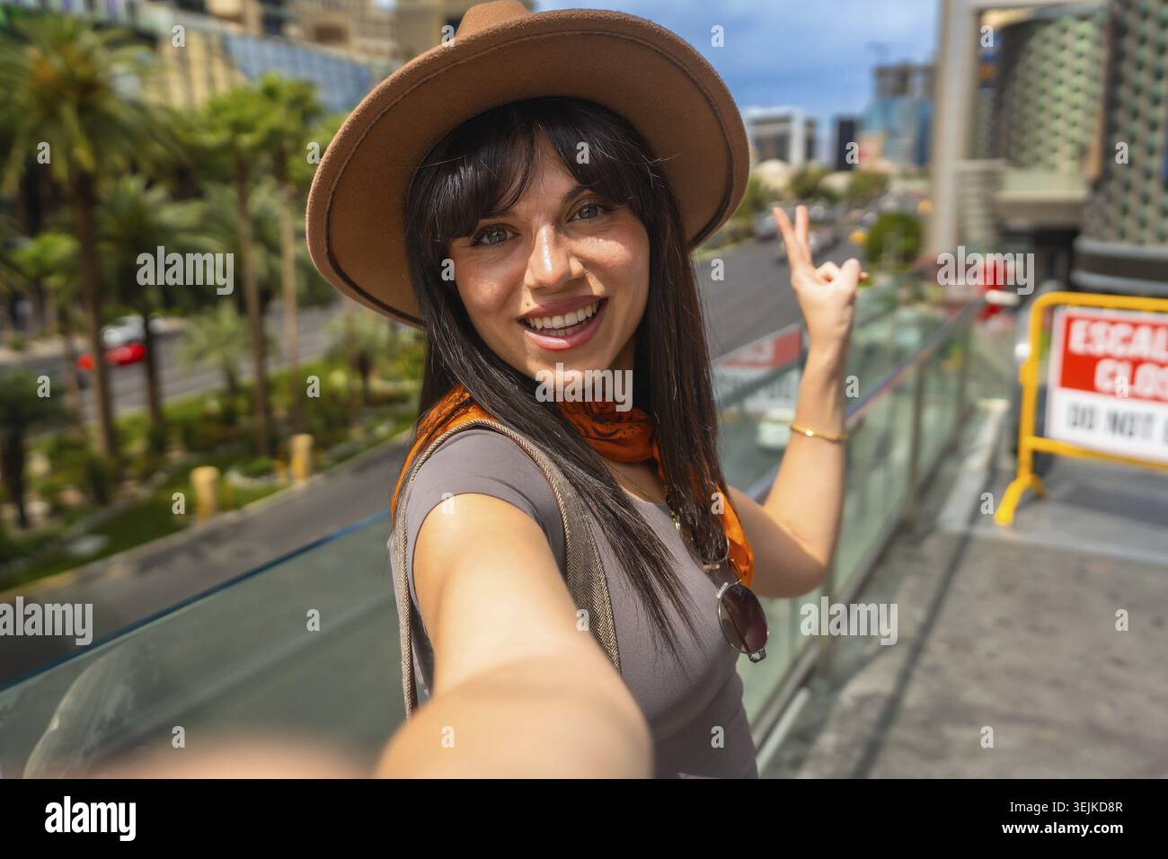 Donna con cappello e sciarpa che si gode la sua vacanza a Las vegas, nevada, sorridendo alla macchina fotografica e facendo un gesto di pace mentre cattura un memorabile Foto Stock