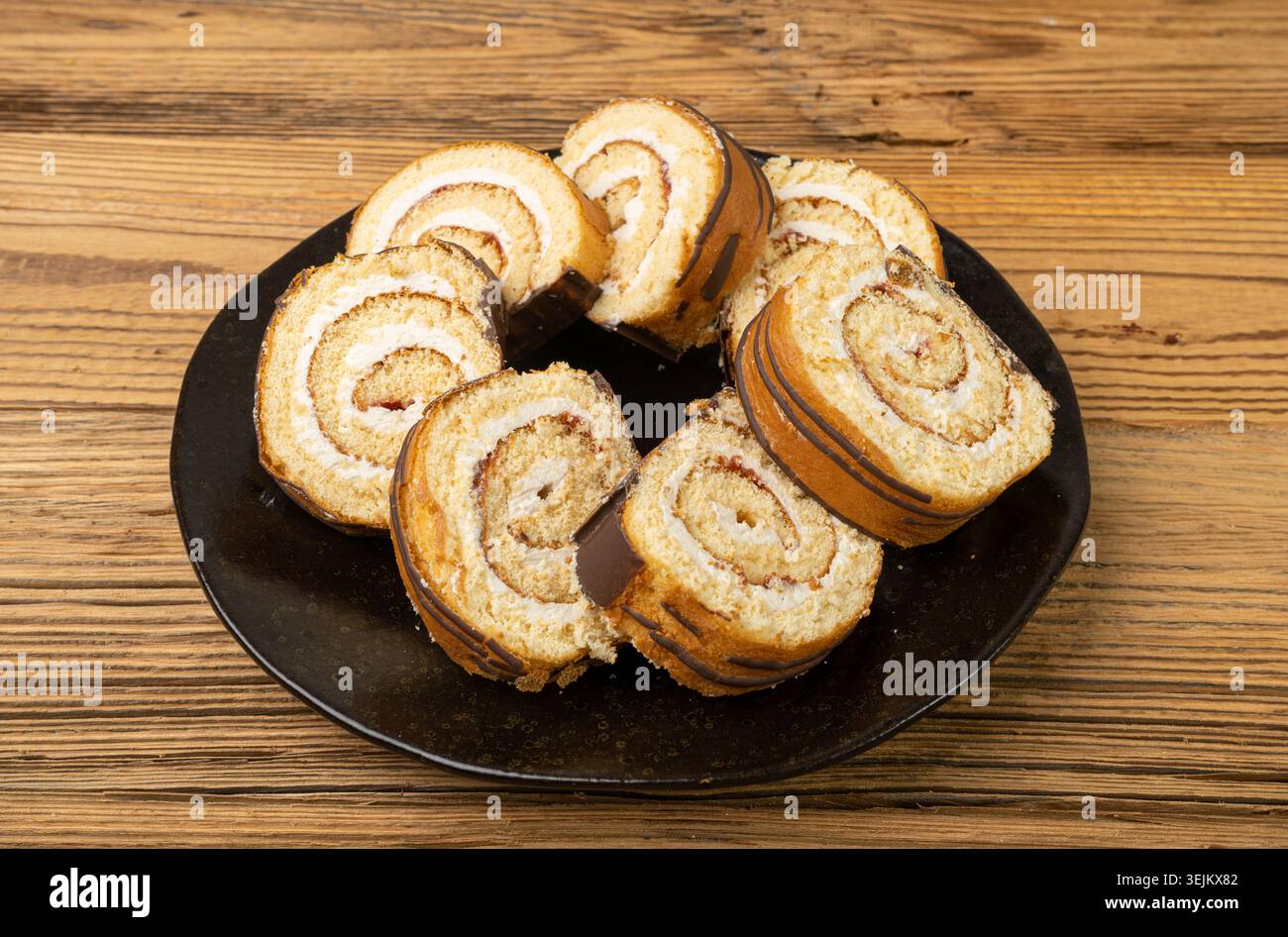 Rotolo svizzero, torta in spugna rotonda, biscotto alla vaniglia arrotolata a fette con ripieno di marmellata, dessert svizzero, torta di tronchi su sfondo legno Foto Stock