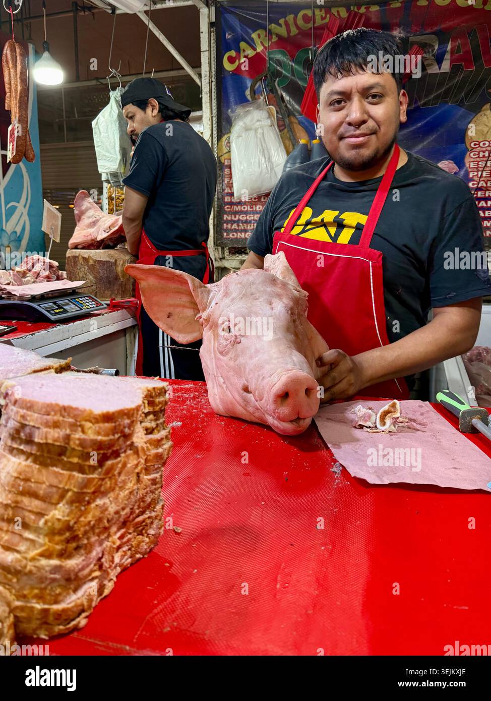 Un macellaio tiene la testa di un maiale in un chiosco di carne a Mercado de la Merced, città del Messico, Messico - Immagine stock catturata con smartphone