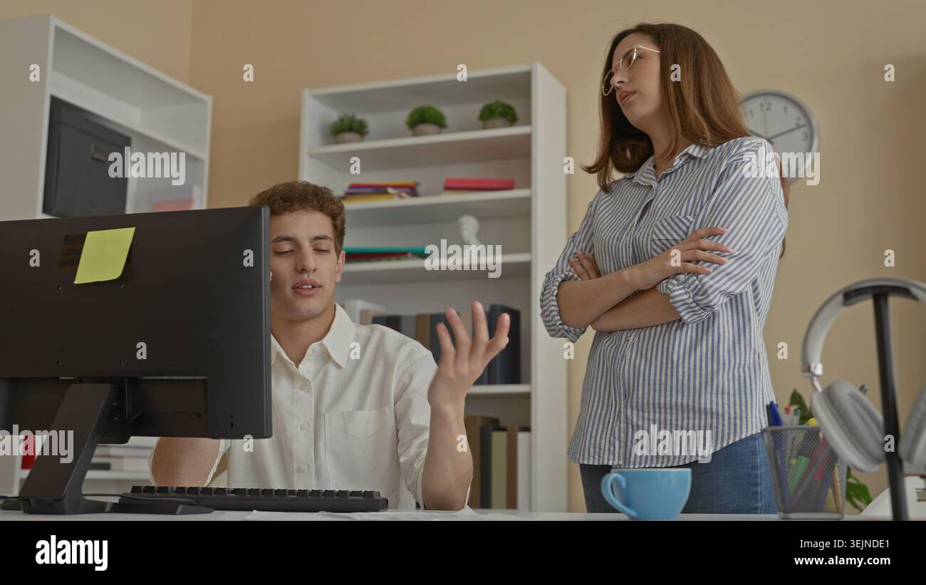 Uomo al computer che parla al telefono mentre la donna sta con mano in fronte nell'edificio dell'ufficio; collaborazione frustrante. Foto Stock