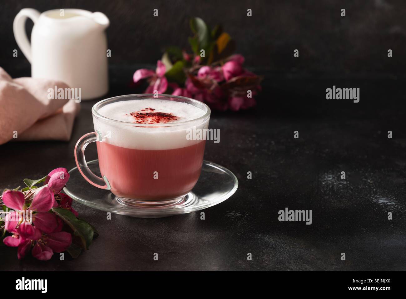 Latte matcha rosa con fiori sakura decorati a polvere su sfondo nero. Foto Stock