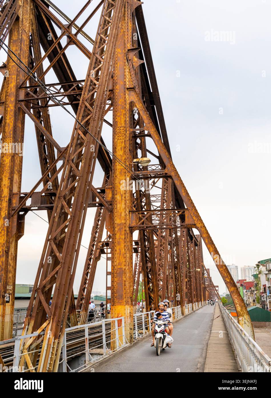 Vietnam-11 giugno 2025: I pendolari nei giorni feriali in moto viaggiano su stretti sentieri, su entrambi i lati del vecchio ponte coloniale francese in acciaio, che attraversa la R di Hanoi Foto Stock