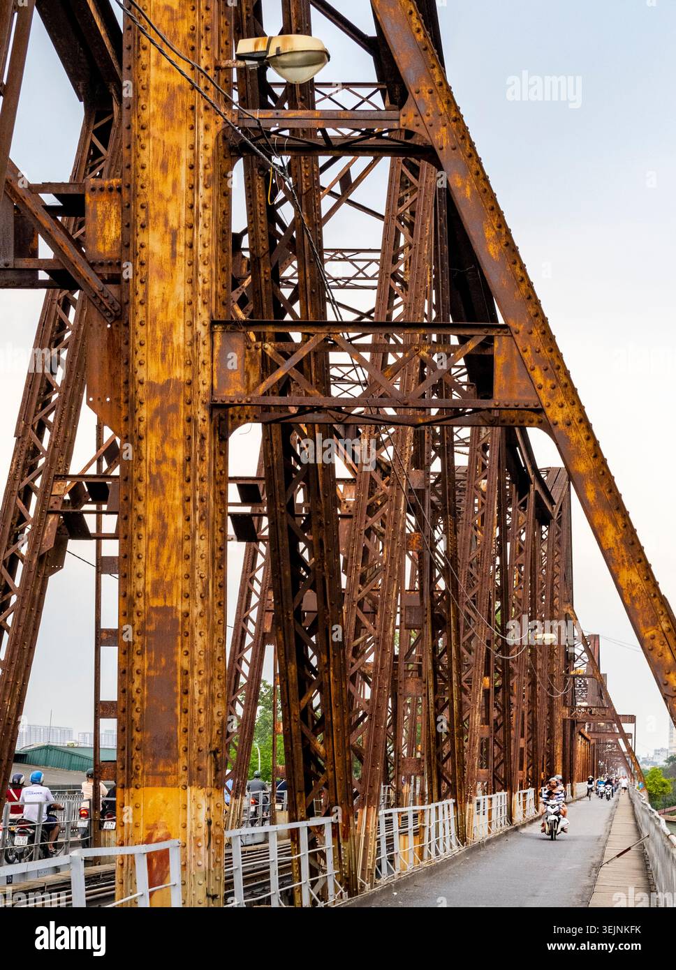 Vietnam-11 giugno 2025: I pendolari nei giorni feriali in moto viaggiano su stretti sentieri, su entrambi i lati del vecchio ponte coloniale francese in acciaio, che attraversa la R di Hanoi Foto Stock