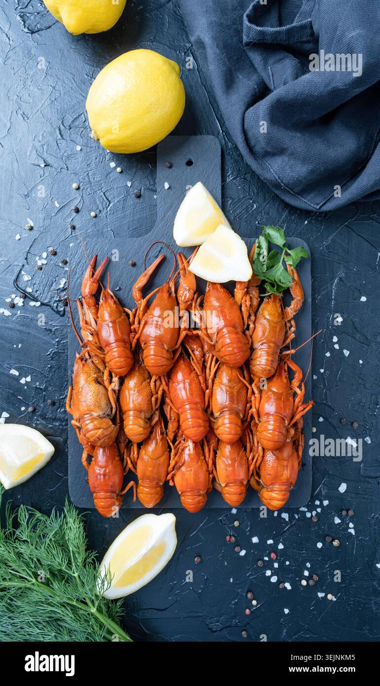 Gamberi cotti su piatto con limoni e spezie su sfondo scuro Foto Stock