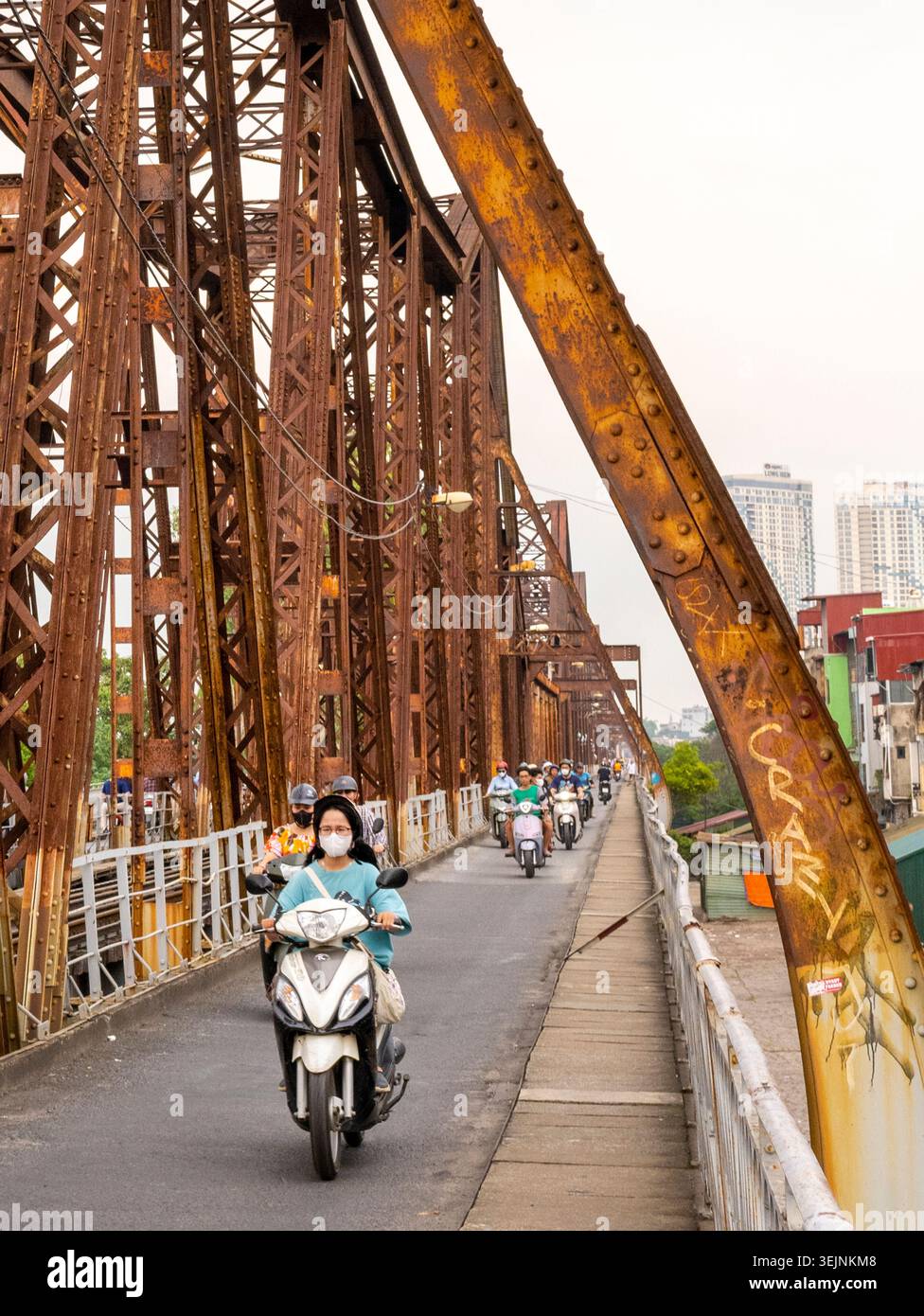 Vietnam-11 giugno 2025: I pendolari nei giorni feriali in moto viaggiano su stretti sentieri, su entrambi i lati del vecchio ponte coloniale francese in acciaio, che attraversa la R di Hanoi Foto Stock