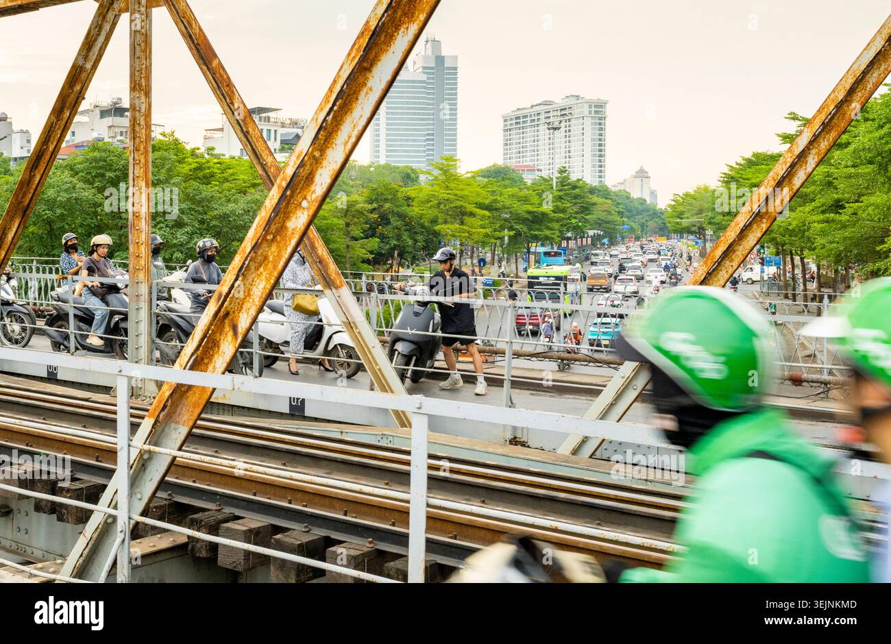Vietnam-11 giugno 2025: I pendolari nei giorni feriali in moto viaggiano su stretti sentieri, su entrambi i lati del vecchio ponte coloniale francese in acciaio, che attraversa la R di Hanoi Foto Stock