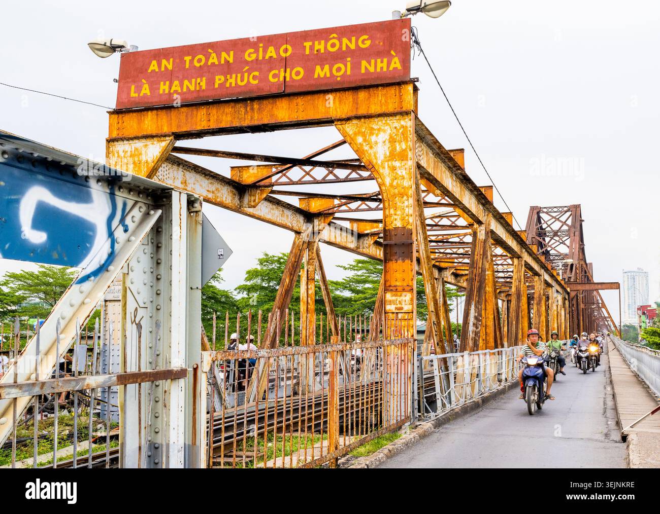 Vietnam-11 giugno 2025: I pendolari nei giorni feriali in moto viaggiano su stretti sentieri, su entrambi i lati del vecchio ponte coloniale francese in acciaio, che attraversa la R di Hanoi Foto Stock