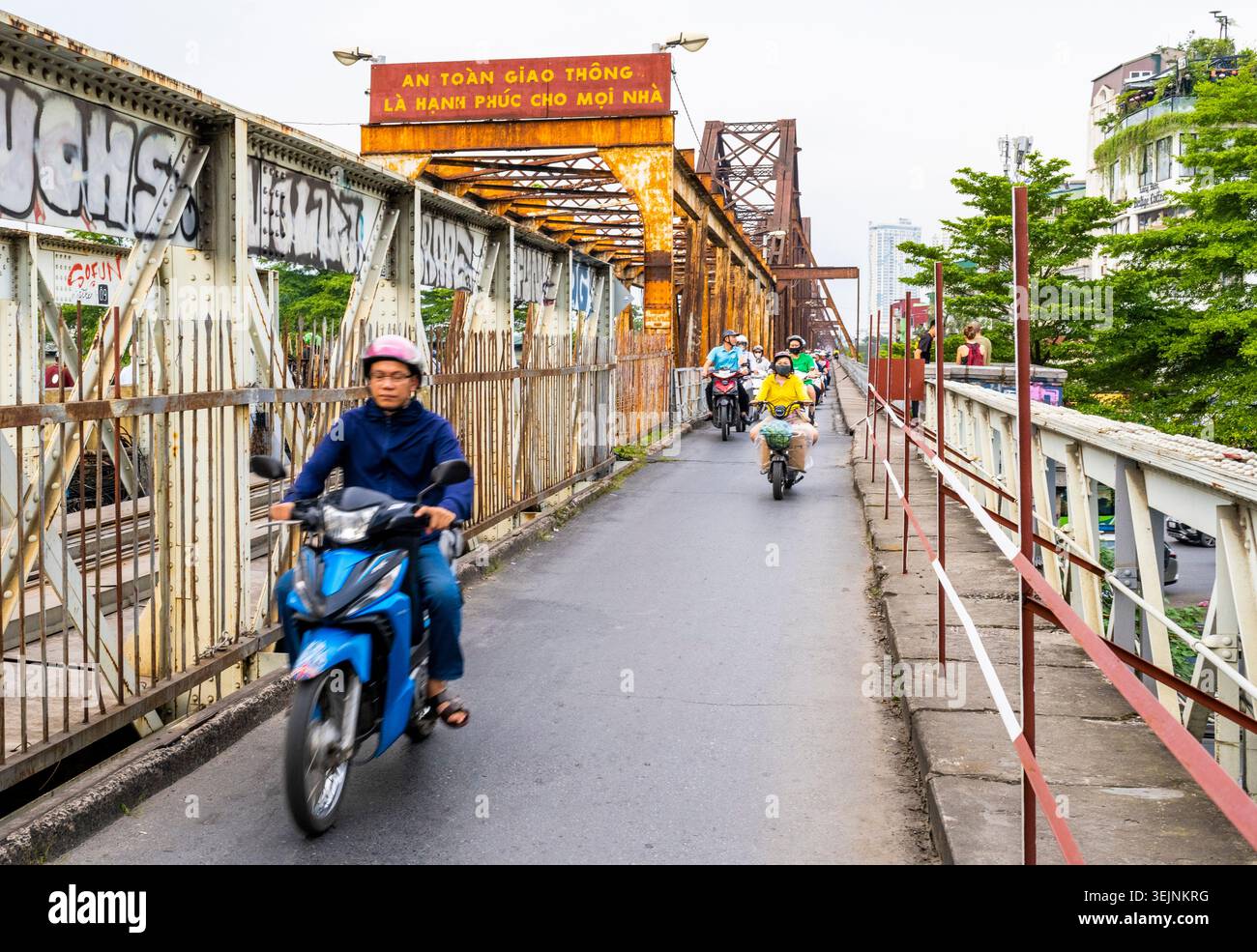Vietnam-11 giugno 2025: I pendolari nei giorni feriali in moto viaggiano su stretti sentieri, su entrambi i lati del vecchio ponte coloniale francese in acciaio, che attraversa la R di Hanoi Foto Stock