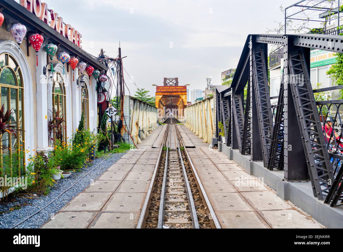 Vietnam-11 giugno 2025: Accanto al popolare Hoa Xa Cafe, un singolo binario ferroviario conduce attraverso il ponte in acciaio, che attraversa il fiume Rosso di Hanoi. Foto Stock