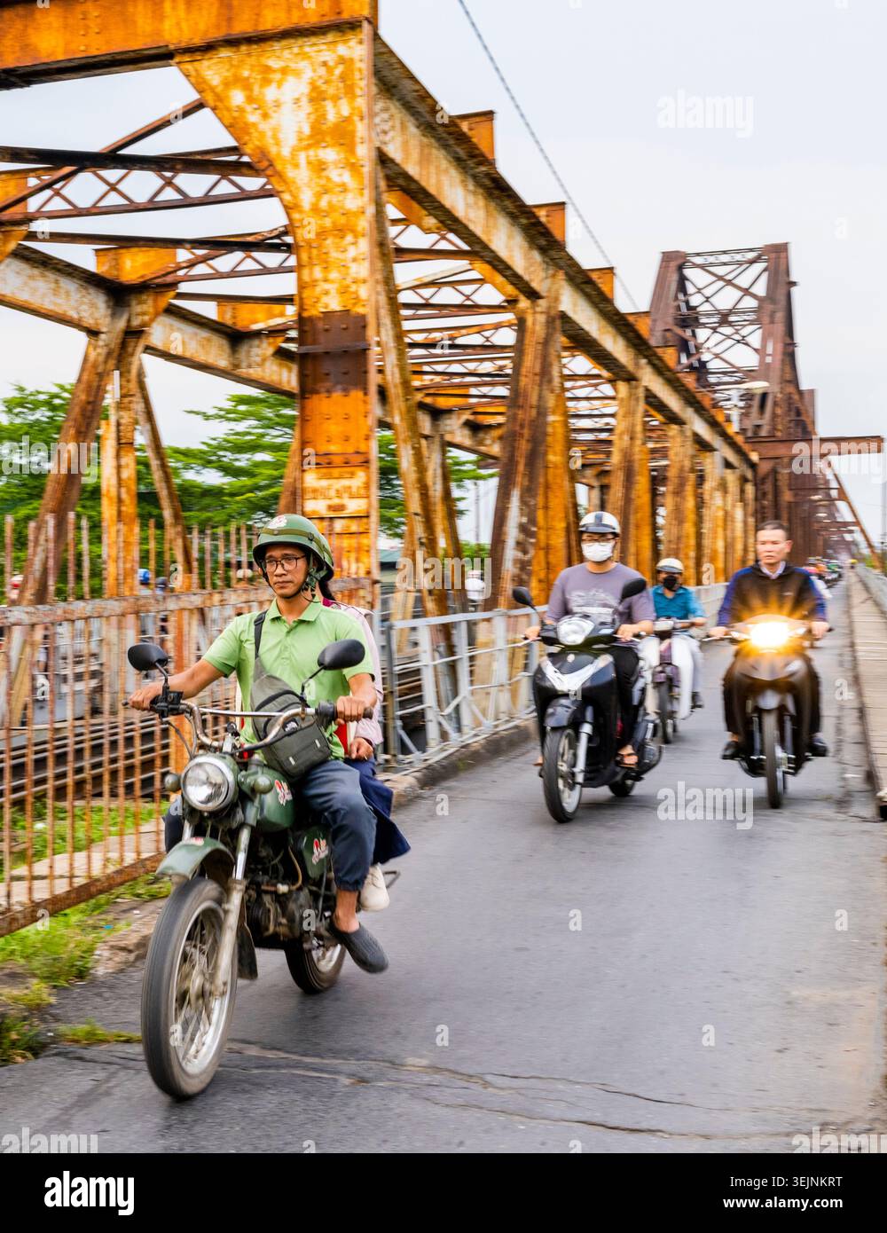 Vietnam-11 giugno 2025: I pendolari nei giorni feriali in moto viaggiano su stretti sentieri, su entrambi i lati del vecchio ponte coloniale francese in acciaio, che attraversa la R di Hanoi Foto Stock