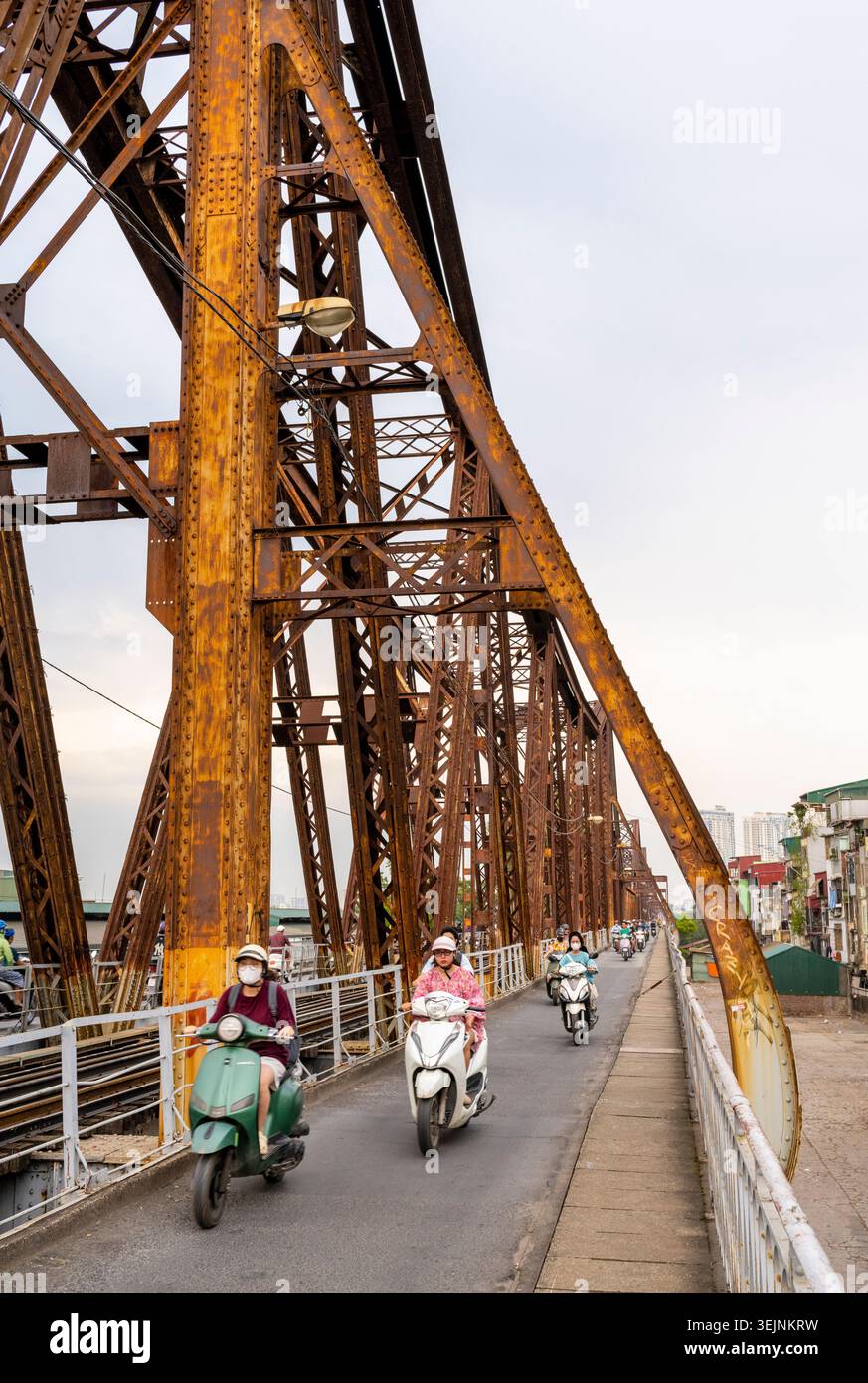 Vietnam-11 giugno 2025: I pendolari nei giorni feriali in moto viaggiano su stretti sentieri, su entrambi i lati del vecchio ponte coloniale francese in acciaio, che attraversa la R di Hanoi Foto Stock
