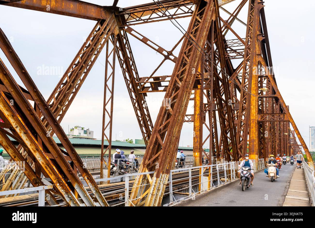 Vietnam-11 giugno 2025: I pendolari nei giorni feriali in moto viaggiano su stretti sentieri, su entrambi i lati del vecchio ponte coloniale francese in acciaio, che attraversa la R di Hanoi Foto Stock